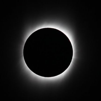 The Moon appears as a black circle, blocking light from the Sun. A faint glow from the Solar corona surrounds the Moon.