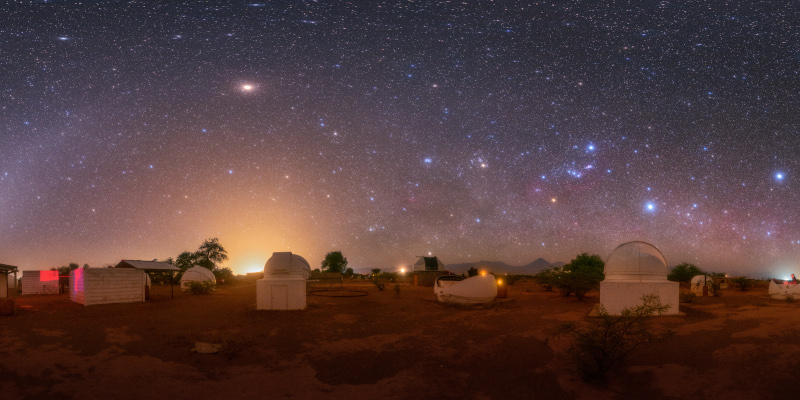 Un gruppo di osservatori di fronte a un cielo buio. Un arco di luce curva dal basso a sinistra. Sono visibili diverse stelle.