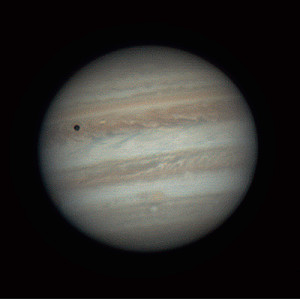 Jupiter with coloured horizontal bands of clouds. The shadow of the moon Io is seen as a dark circle in the top left