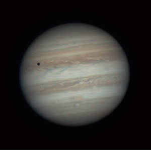 Giove con bande orizzontali di nubi colorate. L'ombra della luna Io è visibile come un cerchio scuro in alto a sinistra.