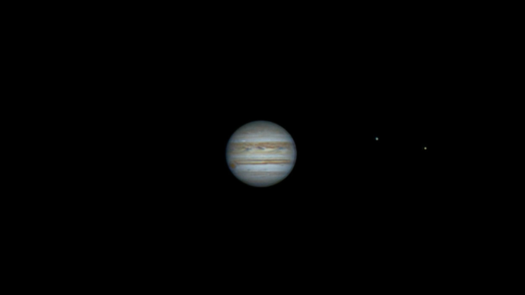 The planet Jupiter with the two of the four Galilean moons (visible as bright dots) orbiting it.