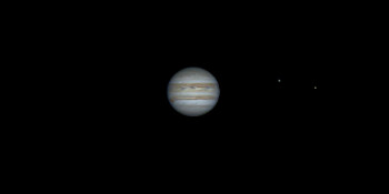 The planet Jupiter with the two of the four Galilean moons (visible as bright dots) orbiting it.