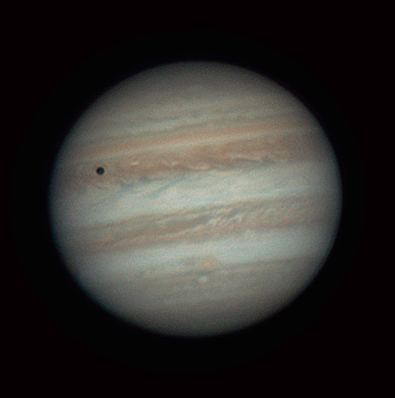 Giove con bande orizzontali di nubi colorate. L'ombra della luna Io è visibile come un cerchio scuro in alto a sinistra.