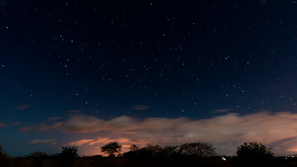 Sternhimmel über einer wolkenverhangenen Landschaft. Links der helle rote Stern Antares