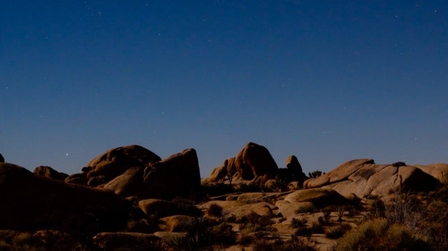 Ein dunkler Himmel über einer trockenen Wüstenlandschaft. Der hellste Stern im Bild geht links unten auf.