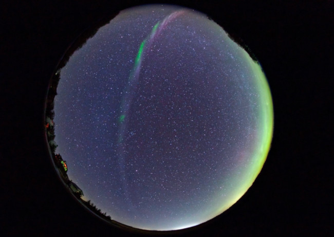 An all-sky image with the sky as a dark blue circle. A curved band of light stretches from top to bottom