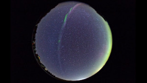 An all-sky image with the sky as a dark blue circle. A curved band of light stretches from top to bottom