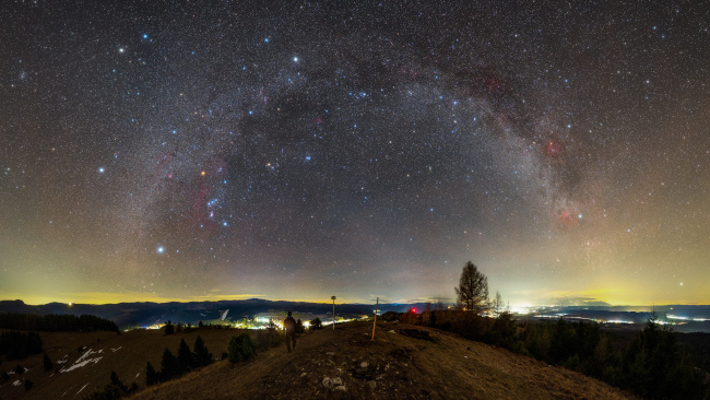 Davanti alla curva della Via Lattea troviamo  Orione a forma di clessidra e il luminoso ammasso stellare delle Pleiadi.