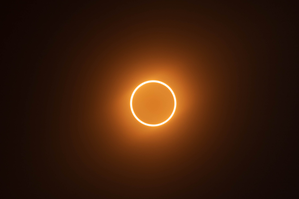 Dark silhouette of the Moon surrounded by a thin, glowing ring of sunlight during an annular solar eclipse.
