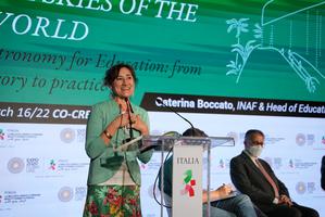 Caterina Boccato gives a speech behind a lectern and in-front of a screen with slides