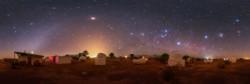 A group of observatories in-front of a dark sky. An arc of light curves from the bottom left. Several stars are visible.