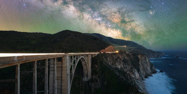 La Via Lattea si staglia su un ponte su una costa scoscesa. In alto a destra  la stella Antares,  rosso intenso e brillante.