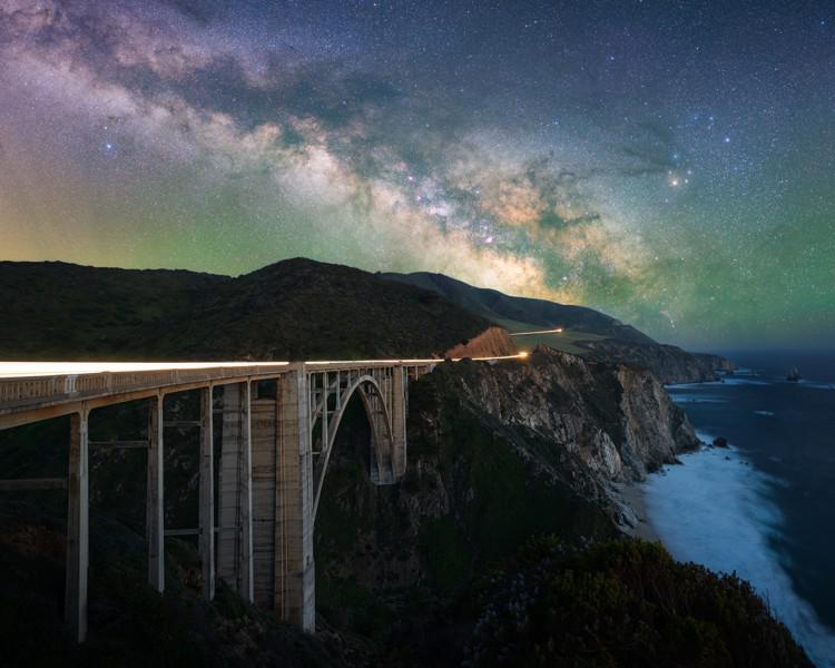 La Via Lattea si staglia su un ponte su una costa scoscesa. In alto a destra  la stella Antares,  rosso intenso e brillante.