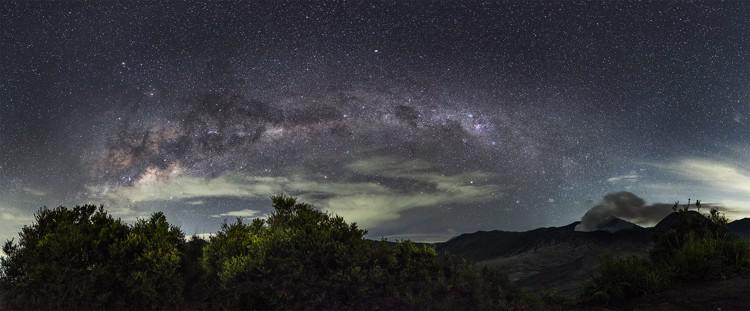 La Via Lattea su un paesaggio nuvoloso. Un triangolo di oggetti luminosi è visibile sulla sinistra della foto.