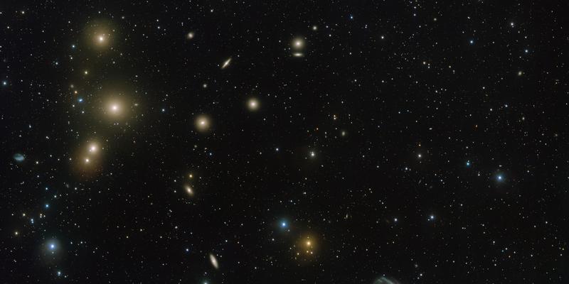 Loose grouping of galaxies with many yellow-ish elliptical galaxies and one priminent spiral galaxy