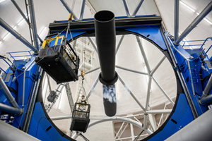 Large curved primary mirror and metal telescope structure at Gemini South. A worker is inspecting the mirror.