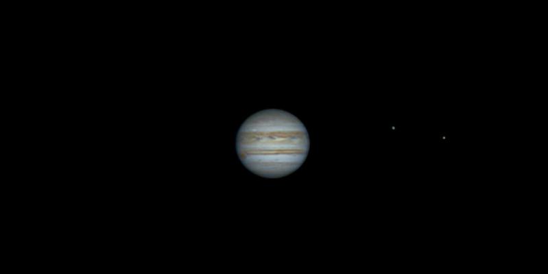 The planet Jupiter with the two of the four Galilean moons (visible as bright dots) orbiting it.