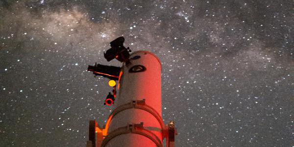 A telescope points to the sky where the Milky Way sits with mottled dark and light patches.