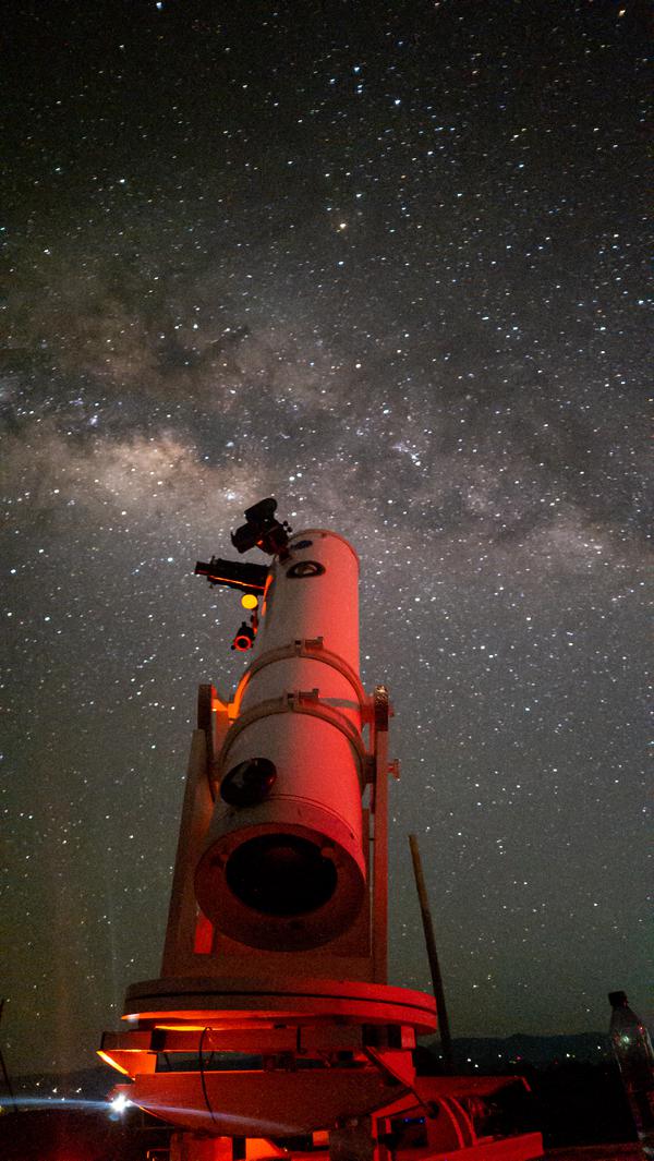 Un telescopio punta il cielo dove la Via Lattea si presenta con macchie scure e chiare.