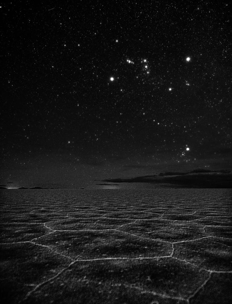 Sopra un paesaggio arido, Orione sembra un papillon. Appena sopra l'orizzonte si trova un ammasso diffuso di stelle luminose.