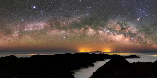 Luce diffusa della Via Lattea rotta da macchie scure. A destra, la stella rossa Antares forma la parte superiore di un gancio