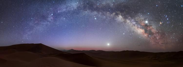 The Milky Way as a bright band over the horizon. The right of the image shows structure of light and dark patches in the band