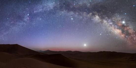 The Milky Way as a bright band over the horizon. The right of the image shows structure of light and dark patches in the band