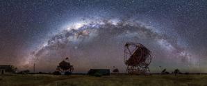 Four dish-shaped telescopes point at the sky with the arc of the Milky Way overhead.