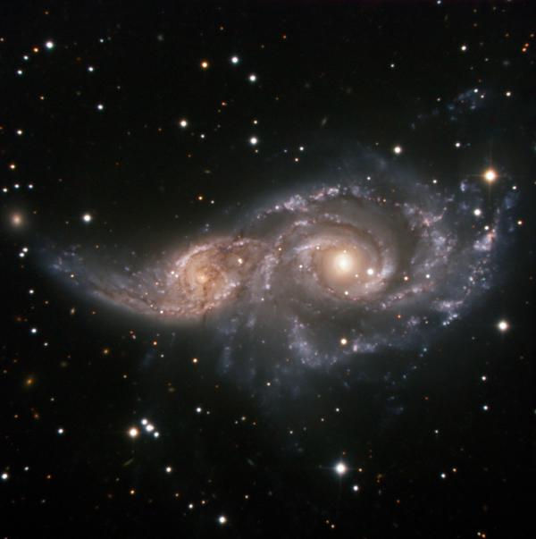 Due galassie a spirale abbracciate nelle prime fasi di fusione, con distorsioni visibili sulla galassia più piccola