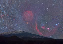 Al di sopra di un vulcano, Orione a forma di farfalla è costellato da luminose strisce di gas nebulari.