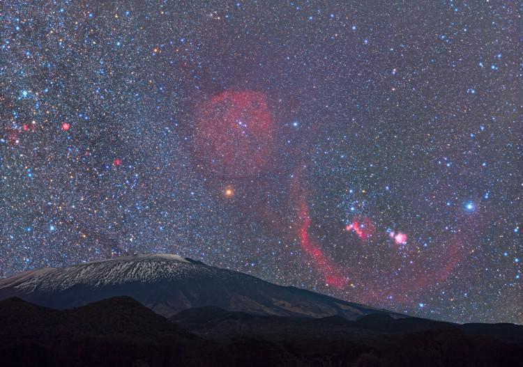 Al di sopra di un vulcano, Orione a forma di farfalla è costellato da luminose strisce di gas nebulari.