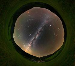 An all-sky image. Bright, slightly curved streaks formed by meteors radiate away from a point in the Milky Way