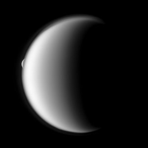 Saturn's moon Titan partially illuminated. Saturn's moon Rhea is partially obscured behind Titan's top left edge