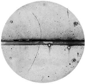 Cloud chamber image showing a dark, curved positron track going from bottom to top. The track crosses a horizontal lead plate