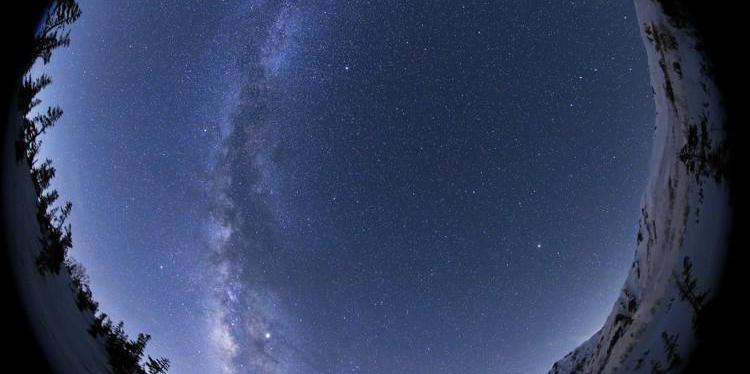 Una foto a tutto cielo della Via Lattea come un fiume diffuso di luce, interrotto da una banda centrale di macchie scure.
