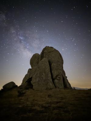 Il debole bagliore della Via Lattea e le sue nubi di polvere screziate dietro un pilastro di roccia.