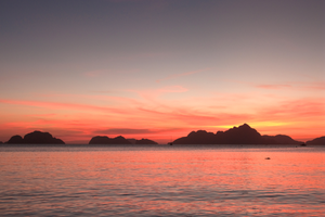 A seascape with calm water, limestone cliffs in silhouette, and a red but fading light sky.