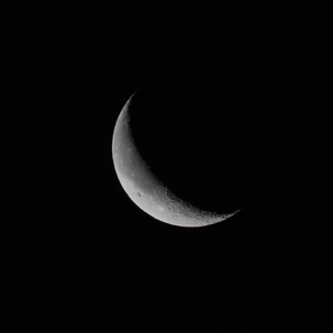 The moon is mostly dark with only a thin bright crescent on the left is visible.