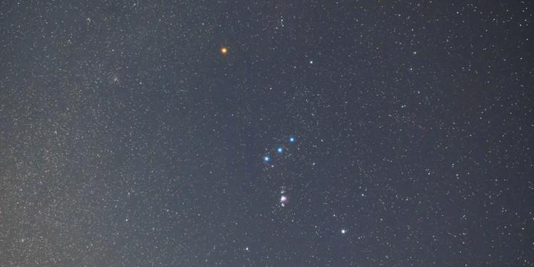 Orion appears as an hourglass with its belt slightly tilted relative to the horizon. The bright star Sirius is bottom-left