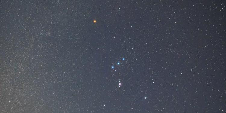 Orion appears as an hourglass with its belt slightly tilted relative to the horizon. The bright star Sirius is bottom-left