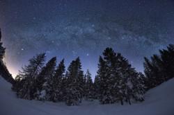 The bright, diffuse Milky Way, interrupted by mottled dark patches, arches over a wintry landscape.